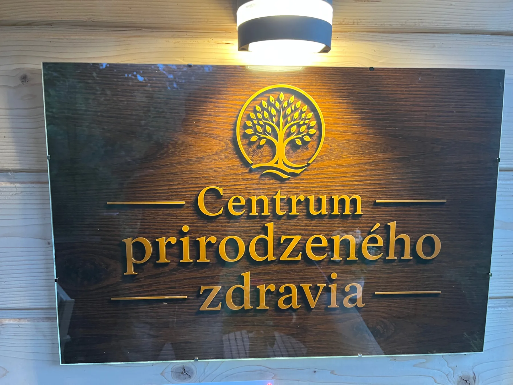 Tabuľa s logom stromu a nápisom Centrum prirodzeného zdravia na drevenej stene